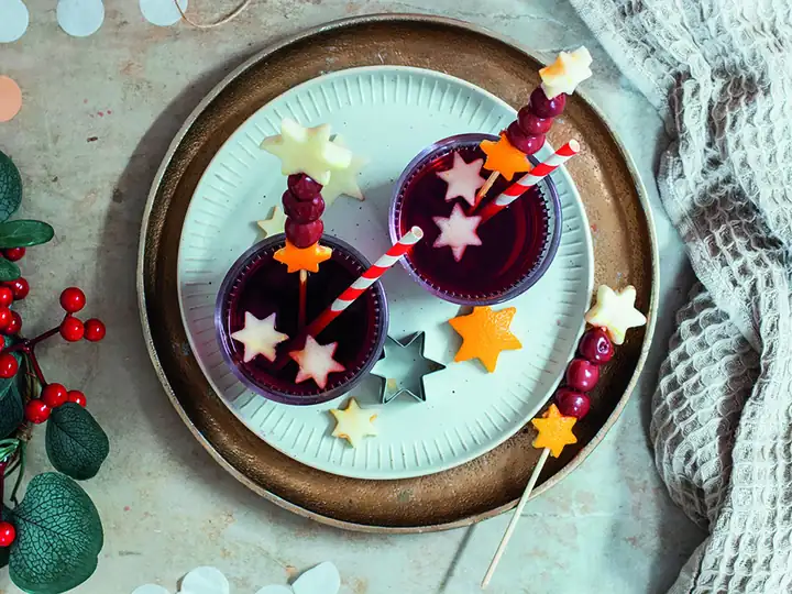 Zwei Gläser roter Kinderpunsch mit Obstspießen aus Kirschen und Sternen aus Apfel und Orange auf einem Teller