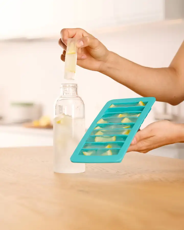 Hand nimmt einen Eiswürfelstick mit Zitrone aus der türkisen Lékué Form über einer Glasflasche