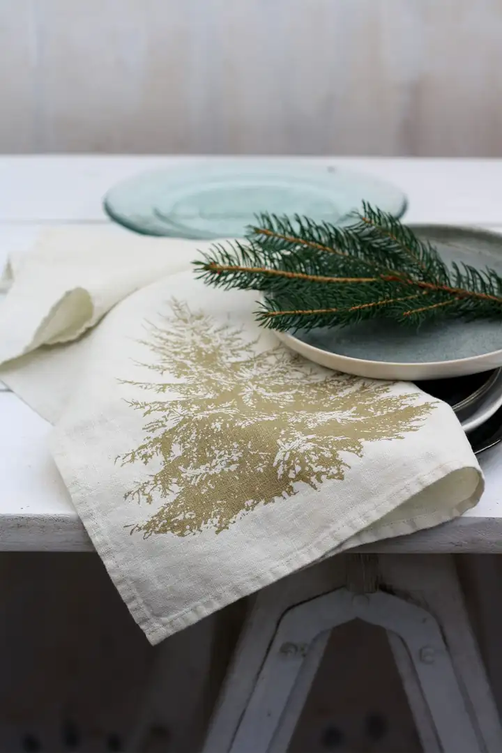 Geschirrtuch Pine von Frohstoff mit Tanne in Messing auf einem gedeckten Tisch