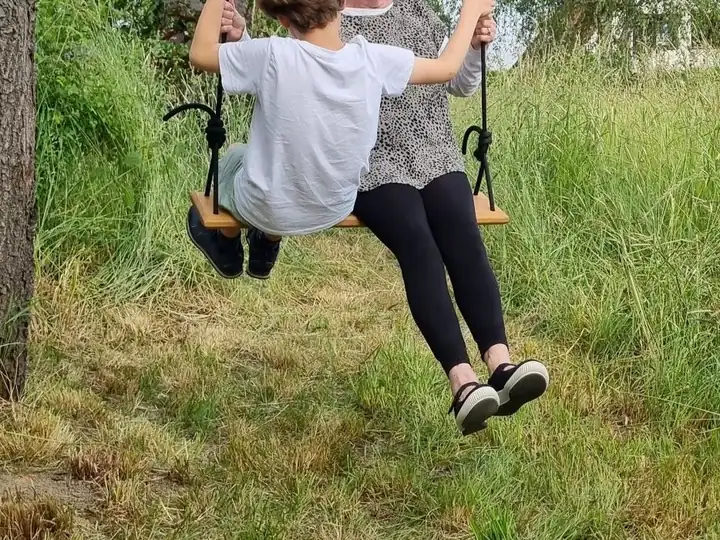 Ein Kind und eine Erwachsene sitzen zusammen auf dem Eichenbrett der Schaukel an einem Baum im Garten
