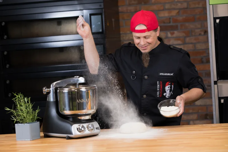Bäckermeister Axel Schmitt mit roter Kappe wirft Mehl über eine Ankarsrum Assistent Original