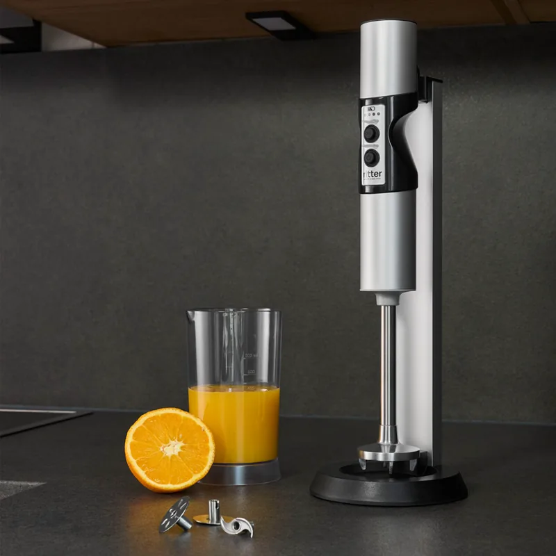 Kabelloser Stabmixer opus 7 von ritterwerk in seiner Ladestation neben einem Glas Orangensaft