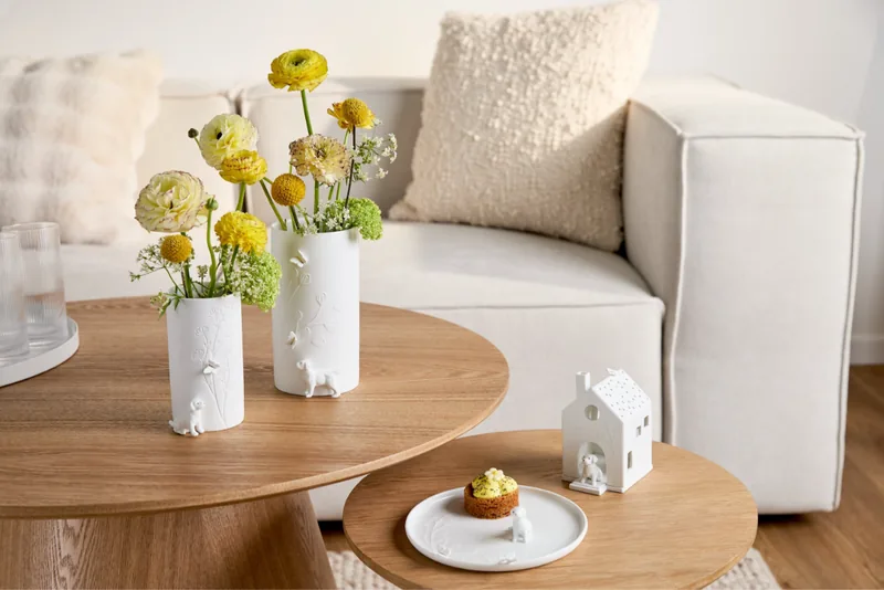 Porzellanvasen mit Blumen, ein Lichthaus und ein Teller von räder auf einem runden Couchtisch