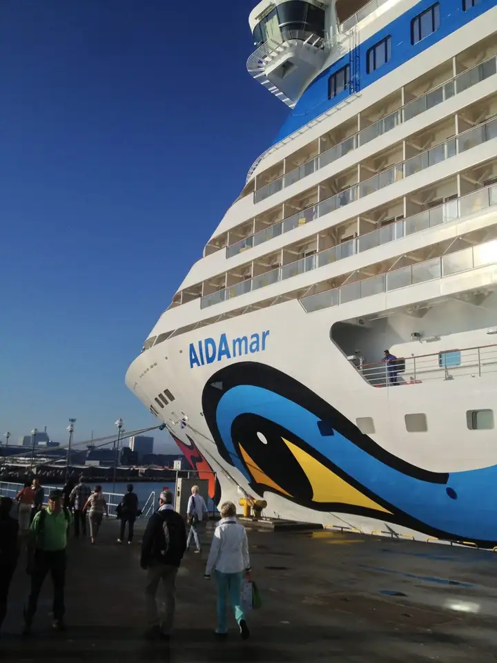 Bug der AIDAmar mit Kussmund und blauen Wellen am Kai in Tallinn, davor Passagiere auf dem Pier