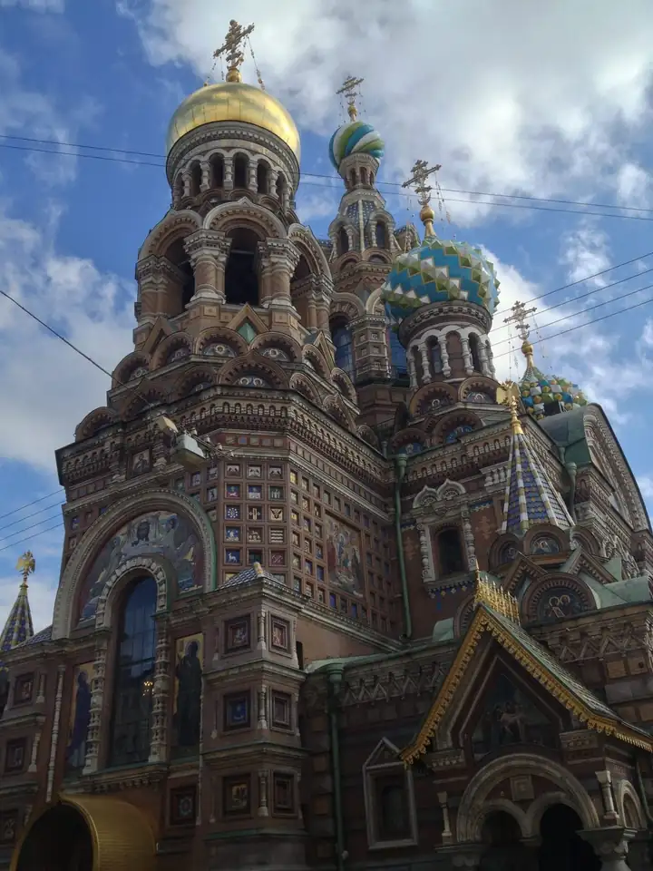 Bunte Zwiebeltürme der Erlöserkirche in St. Petersburg vor blauem Himmel mit Wolken