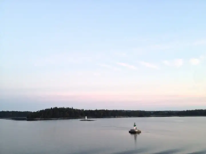 Ruhige Ostsee in der Abenddämmerung mit einer bewaldeten Insel, einem kleinen Leuchtturm und einem Boot