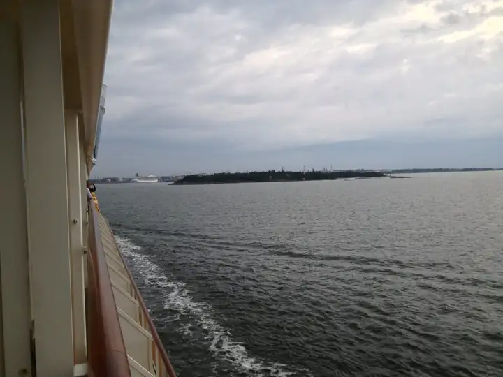 Blick vom Schiff auf Schären und eine bewaldete Insel vor Helsinki unter grauen Wolken
