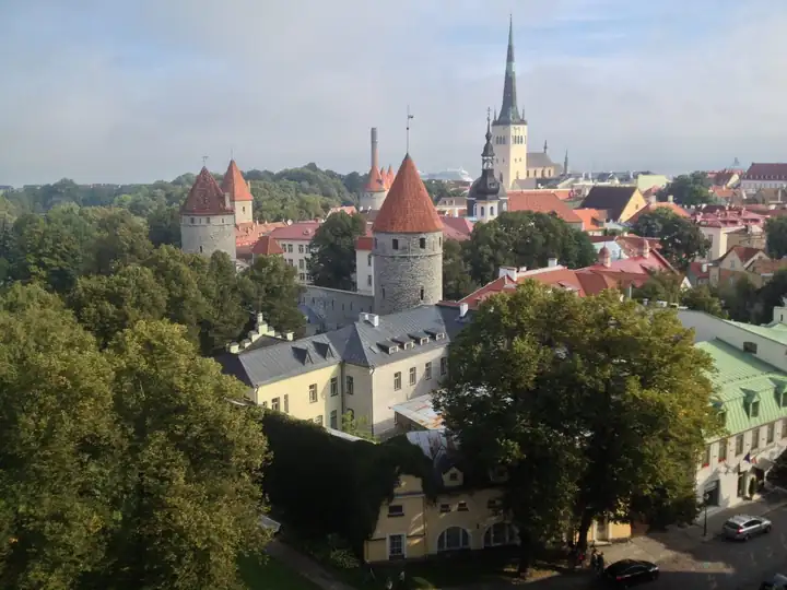 Rote Dächer und runde Wehrtürme der Stadtmauer von Tallinn, dahinter die Spitze der Olaikirche