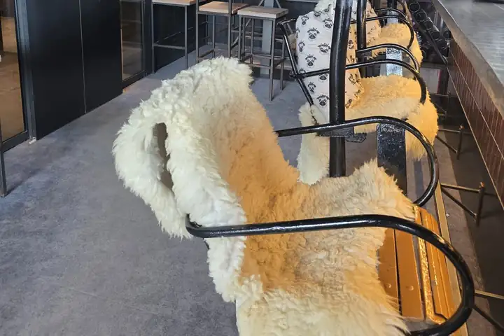 Sitze eines alten Sessellifts mit Lammfell und schwarzem Metallbügel hängen an einer Theke aus Holz, dahinter ein Kissen mit Mopsmuster