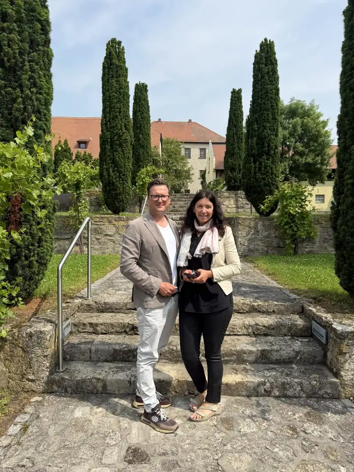 Lars Laschinski und Christine Klauder auf einer Steintreppe zwischen Säulenzypressen, dahinter das Schloss