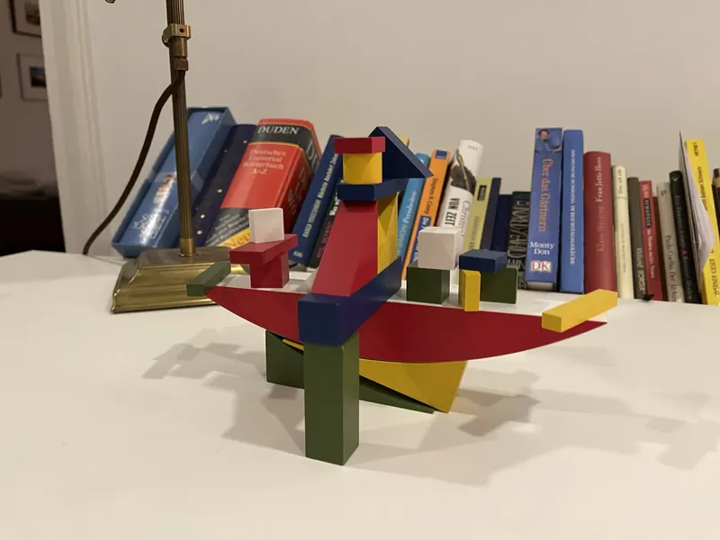 Bauhaus Bauspiel als bunter Aufbau auf einem weißen Tisch vor einem Bücherregal, links der Fuß einer Messinglampe