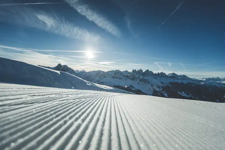 Frisch präparierte Piste auf der Plose in der Sonne, dahinter die Dolomiten