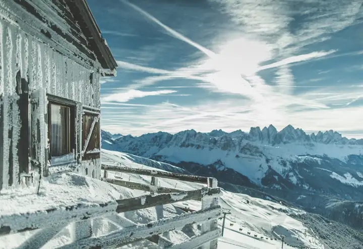 Verschneite Holzhütte auf der Plose mit Blick auf die Dolomiten unter blauem Himmel