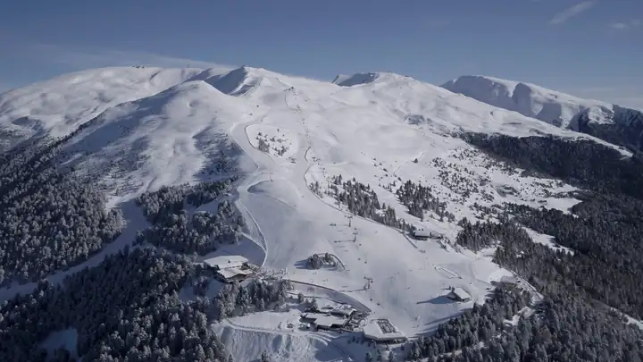 Die verschneite Plose von oben mit Pisten und Wald