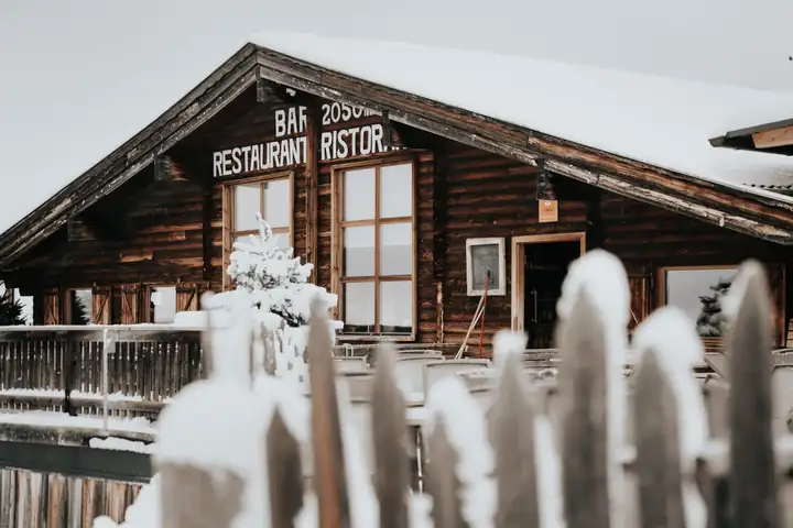 Holzhütte mit der Aufschrift Bar Restaurant und 2050 m im Schnee, davor ein verschneiter Lattenzaun