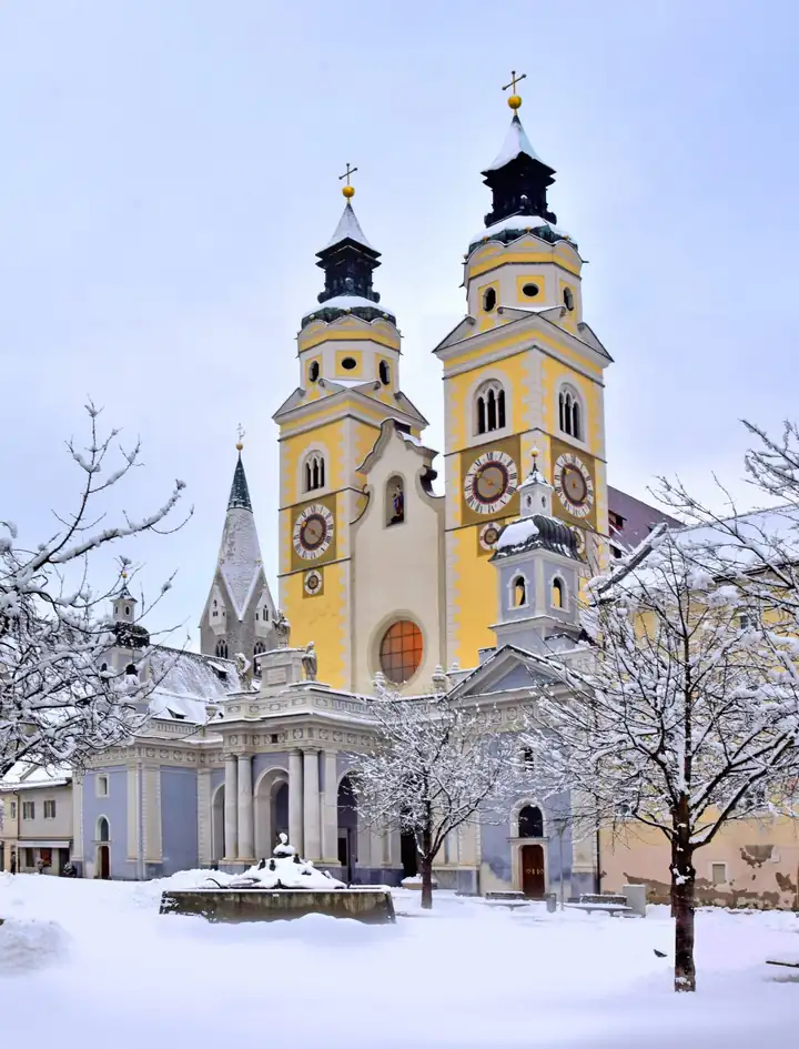 Der Brixner Dom mit zwei gelben Türmen im Schnee, davor der verschneite Domplatz