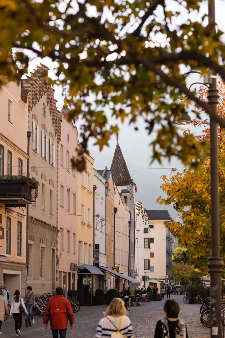 Altstadtgasse in Brixen im Herbst mit bunten Hausfassaden, Laternen und Passanten unter gelbem Laub
