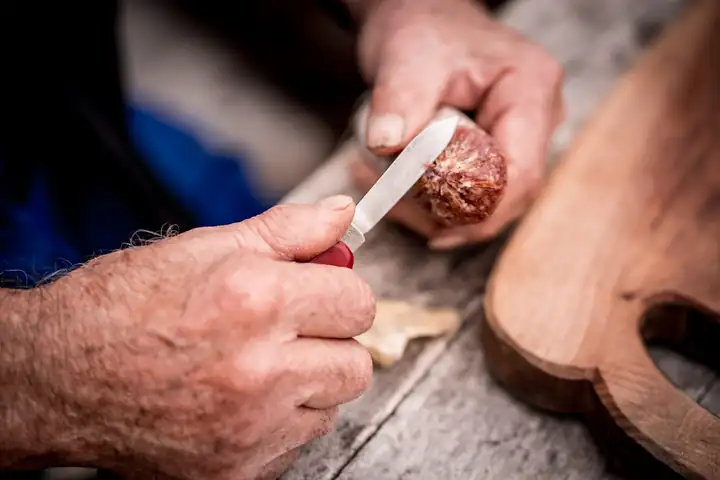 Hände schneiden mit einem kleinen Messer eine Wurst auf einem Holzbrett