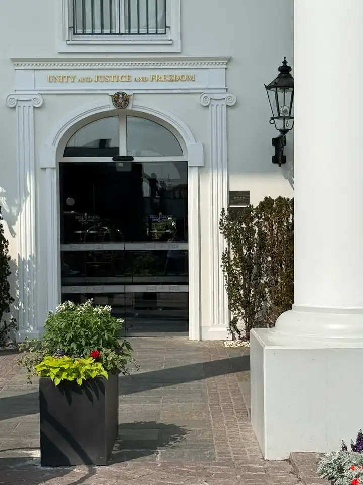 Weiße Eingangstür des Hotels Bell Rock unter einem Bogen mit ionischen Pilastern, darüber in Gold die Worte Unity and Justice and Freedom, rechts eine Laterne und das Schild mit vier Sternen