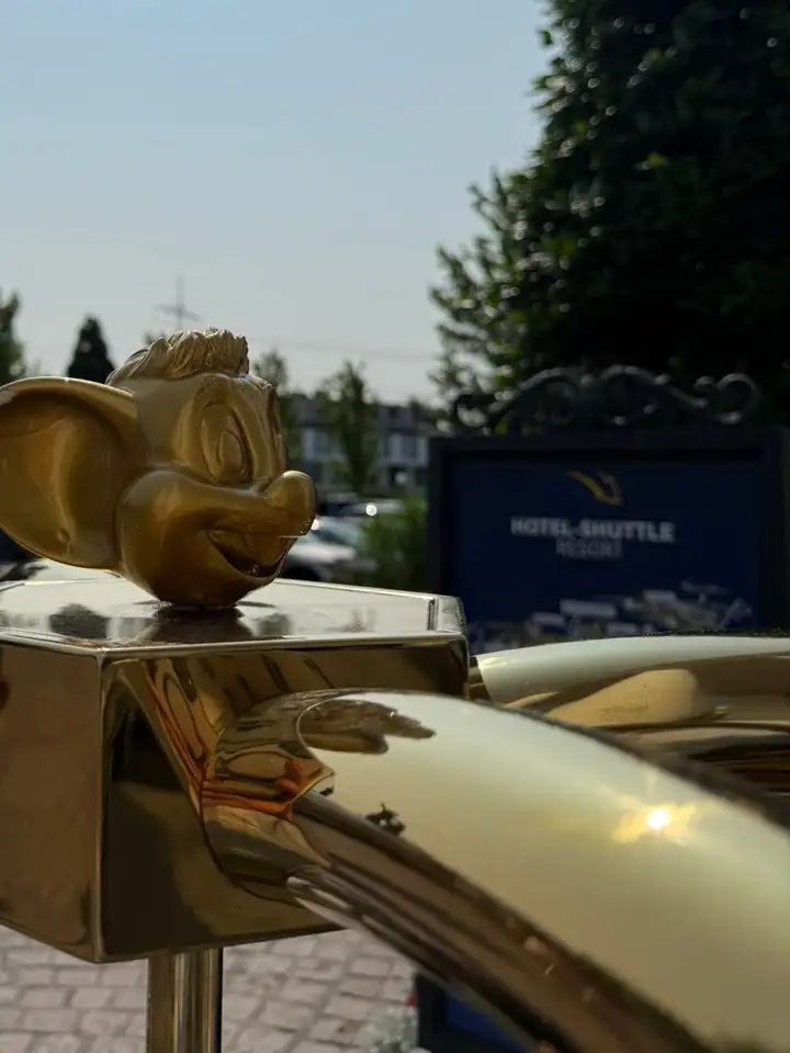 Goldener Kopf von Ed Euromaus auf einem Gepäckwagen aus Messing, dahinter ein Schild mit der Aufschrift Hotel Shuttle Resort