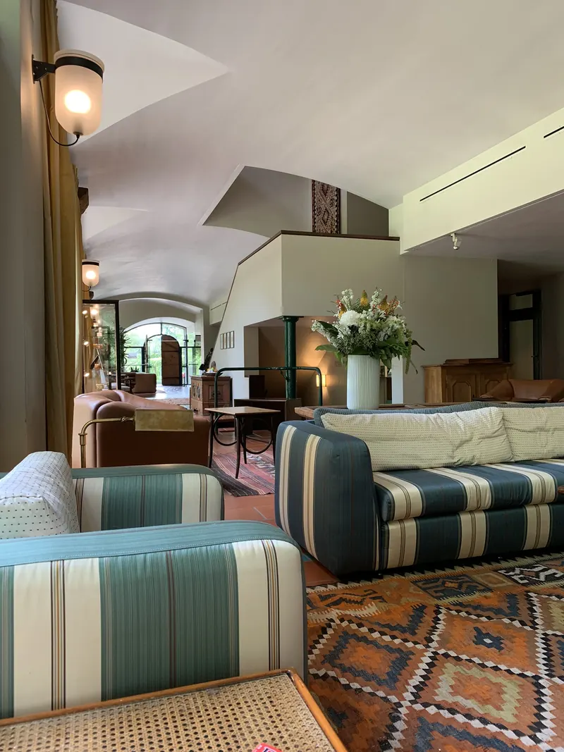 Halle mit gestreiften Sofas in Blau und Grün, einem Teppich mit Rautenmuster, Blumen auf einem Tisch und einem Gewölbe im Hintergrund