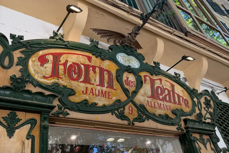 Grün und gold verziertes Ladenschild Forn des Teatre an der Plaça de Weyler in Palma, darüber ein schmiedeeiserner Drache