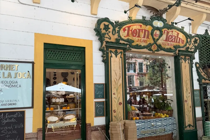 Fassade der Bäckerei Fornet de la Soca an der Plaça de Weyler in Palma mit dem Jugendstilschild Forn des Teatre, grünen Rahmen und Tafeln vor dem Eingang