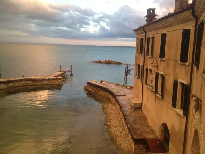Steinmole und kleiner Steg im goldenen Abendlicht vor dem Gardasee, rechts die Fassade mit Fensterläden