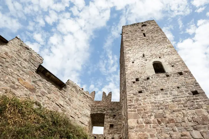 Bergfried und Zinnenmauer von Burg Hocheppan von unten vor blauem Himmel mit Wolken