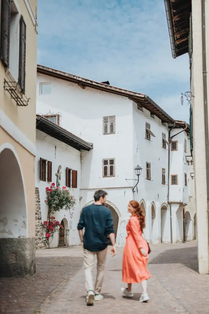 Ein Paar spaziert durch eine Gasse mit Bogengängen und weißen Häusern in der Altstadt von Neumarkt