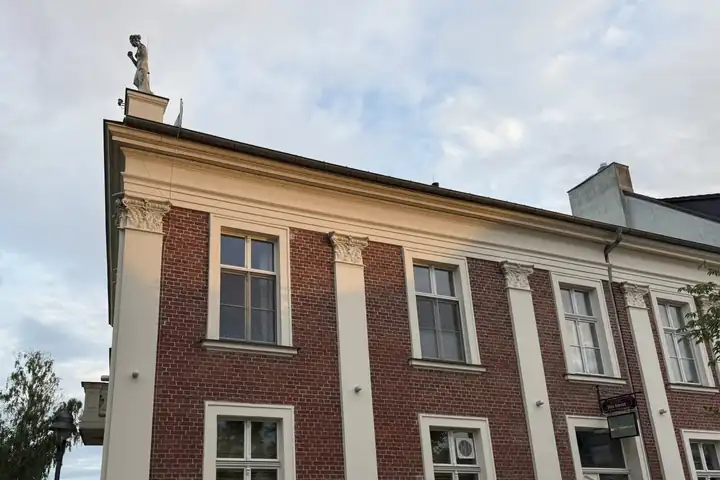 Klassizistisches Haus aus rotem Backstein mit hellen Pilastern und einer Figur auf dem Dach, rechts unten die Schilder des Restaurants