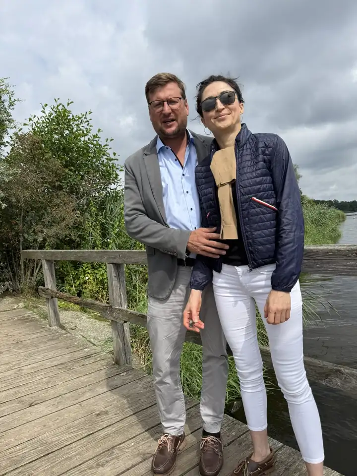 Ein Paar auf einem Holzsteg an der Havel, dahinter Schilf, Büsche und Wasser unter Wolken