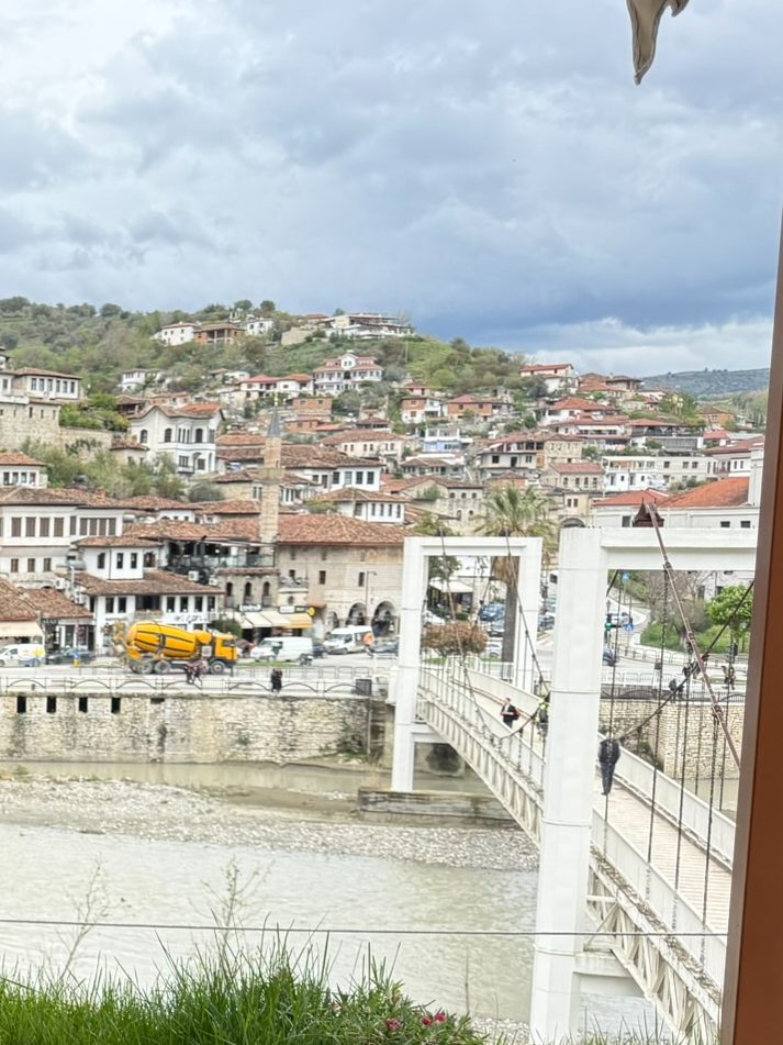 Weiße Häuser mit vielen Fenstern am Hang von Berat, davor der Fluss Osum und eine weiße Fußgängerbrücke