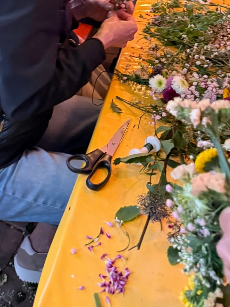 Tisch mit gelber Decke, darauf Wiesenblumen, Schleierkraut, Drahtrollen und eine Schere