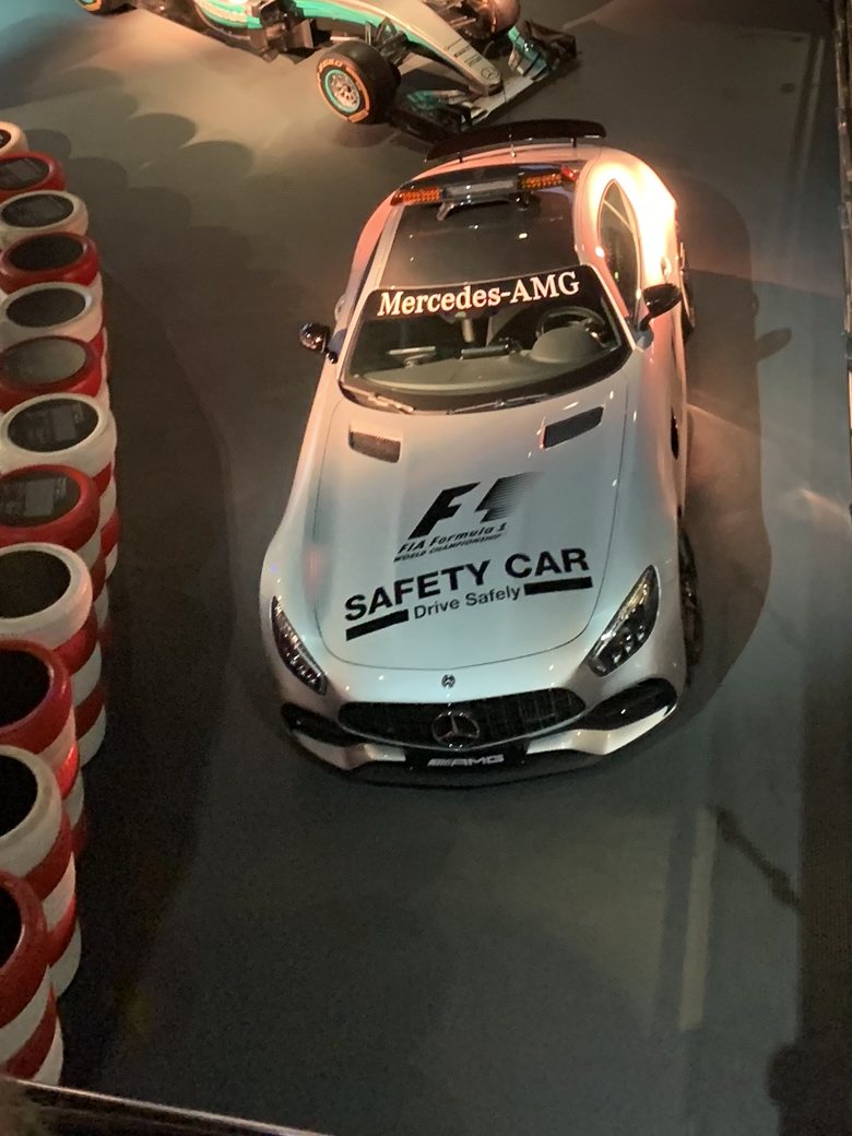 Silbernes Safety Car der Formel 1 von Mercedes AMG zwischen Reifenstapeln in einer Halle, dahinter ein Rennwagen