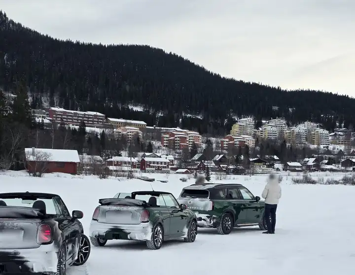 Drei MINI auf dem verschneiten Eis des Åresjön, dahinter der Ort Åre mit roten Holzhäusern und Hotels am bewaldeten Hang