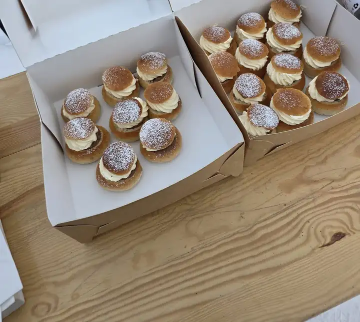 Zwei Pappschachteln voller Semlor mit Sahne und Puderzucker auf einem Holztisch