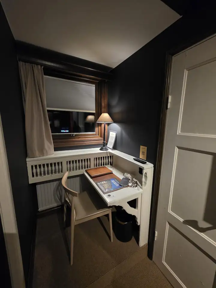 Schmaler Schreibtisch am Fenster mit Lampe, darauf Mappen und das Magazin des Åregården, rechts eine weiße Holztür