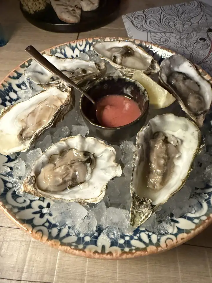 Austern auf Eis in einer Schale mit blauem Muster, in der Mitte eine Sauce