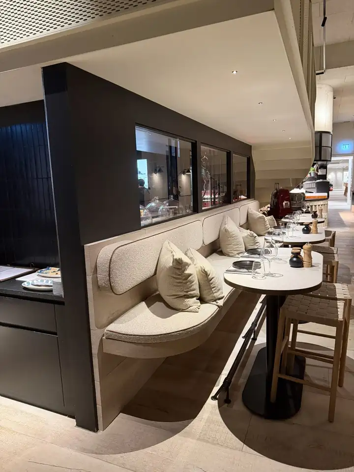 Restaurant BRACA mit Sitzbank in Hellbeige, runden Tischen, dunklen Wänden und Fenstern