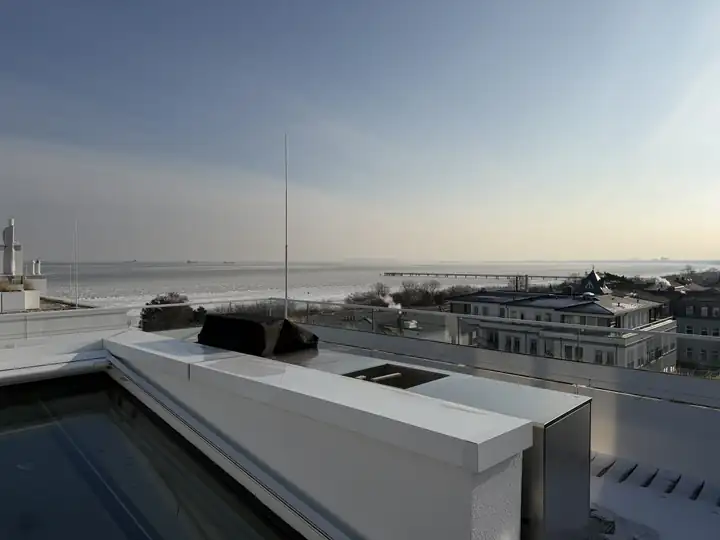 Dachterrasse eines Penthouse mit Whirlpool und Außenküche, dahinter die Dächer von Ahlbeck, die Seebrücke und die vereiste Ostsee