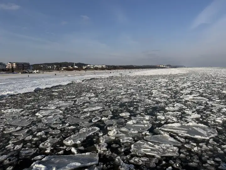 Eisschollen auf der Ostsee vor Ahlbeck, im Hintergrund die Küste mit Häusern unter blauem Himmel