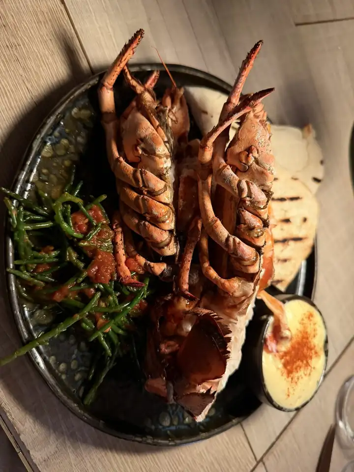 Gegrillte Krustentiere mit Queller und gegrilltem Gemüse auf einem dunklen Teller