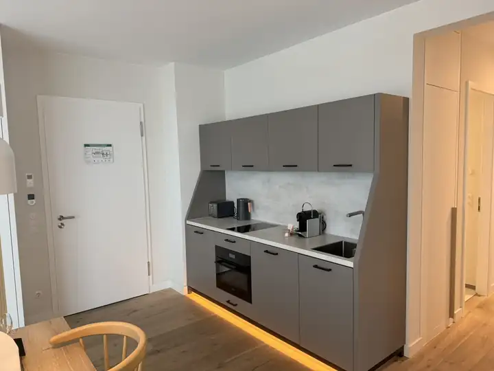 Küchenzeile in Grau mit Backofen, Kochfeld, Kaffeemaschine und Wasserkocher, darunter warmes Licht am Boden