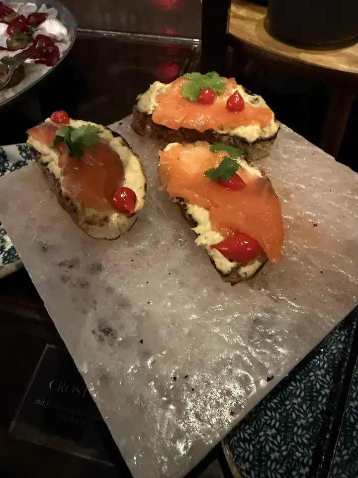 Lachs mit Creme und roten Beeren auf Brot, angerichtet auf einer Platte aus Salzstein