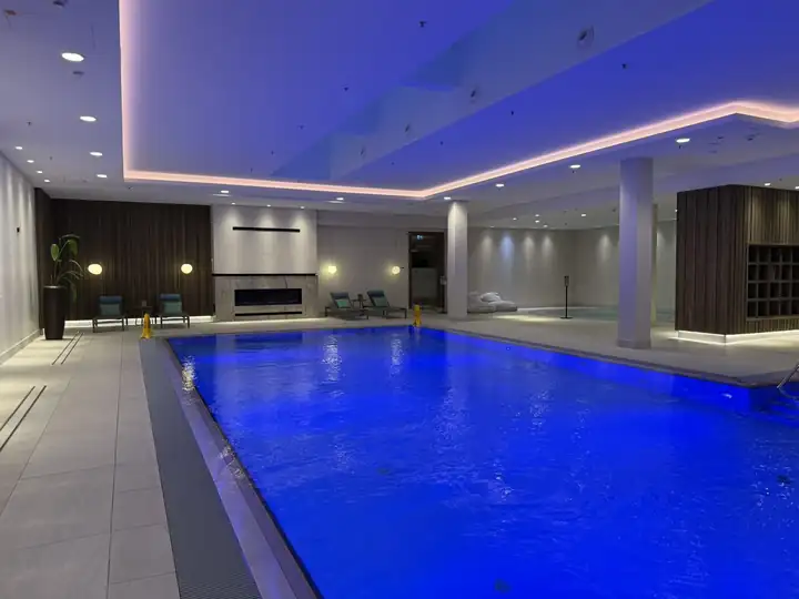 Innenbecken des Spa in blauem Licht, dahinter Liegen, eine Wand mit Kamin und eine Holzwand