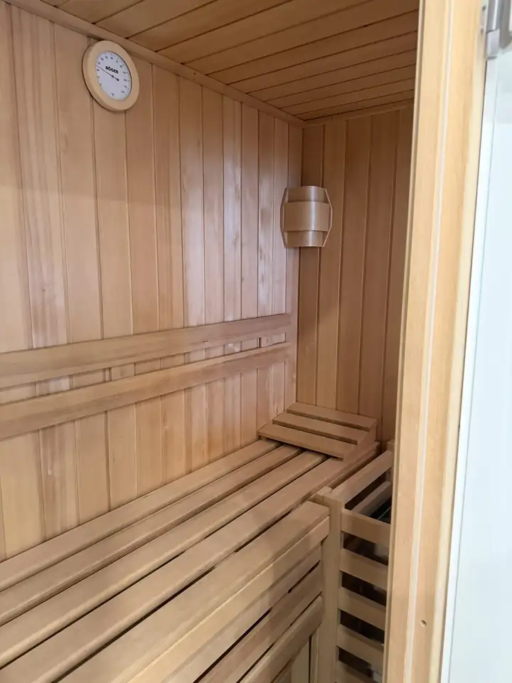 Kleine Sauna aus hellem Holz mit Bänken und Thermometer im Apartment