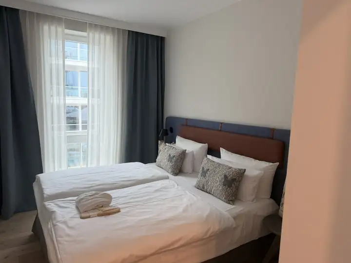 Schlafzimmer mit Doppelbett, Kopfteil aus Leder und Stoff, Kissen mit Muster und Bademänteln auf dem Bett