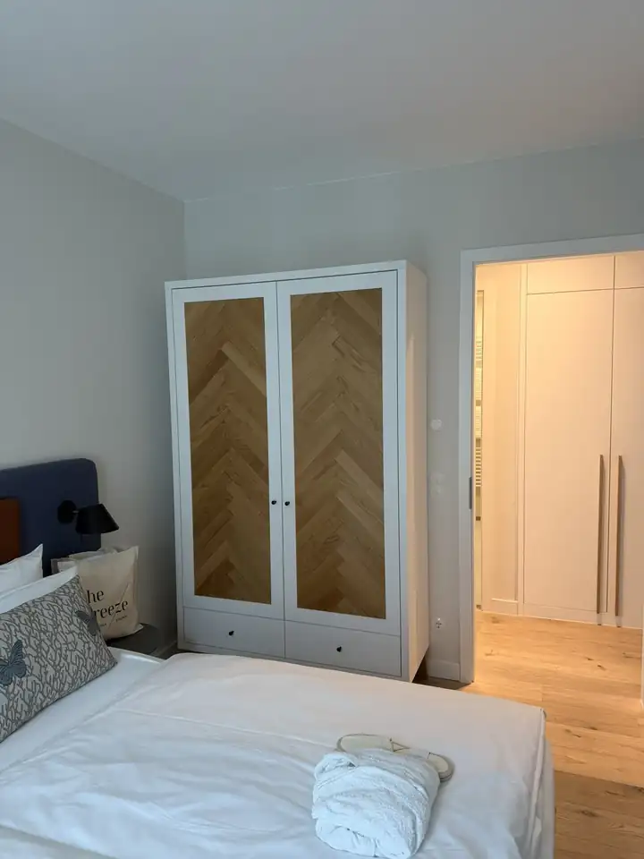 Zweites Schlafzimmer mit weißem Bett und weißem Kleiderschrank mit Türen in Fischgrätmuster aus Holz
