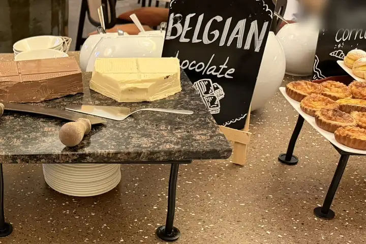 Frühstücksbuffet mit Blöcken aus Milchschokolade und weißer Schokolade auf einer Granitplatte, daneben eine Tafel mit der Aufschrift Belgian chocolate